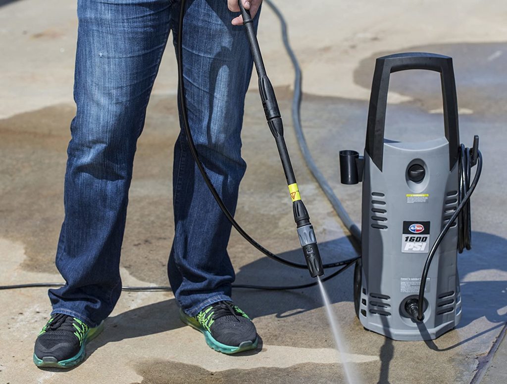Man in blue jeans using a pressure washer too clean concrete