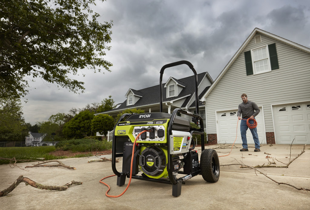 In front of a house, a man holds a cable that runs to the Ryobi fuel-injected generator in the foreground.