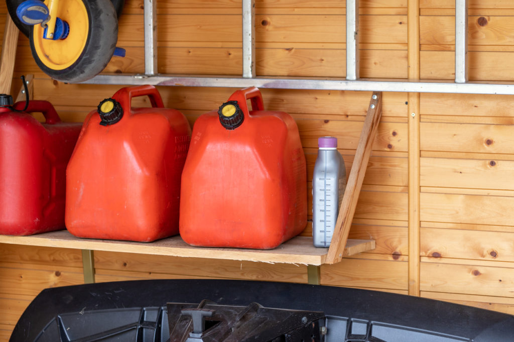 Garage corner with three red plastic fuel cans , staircase and snow plough for atv with wooden wall on background. Petrol gas containers reserves storage at vehicle home garage.