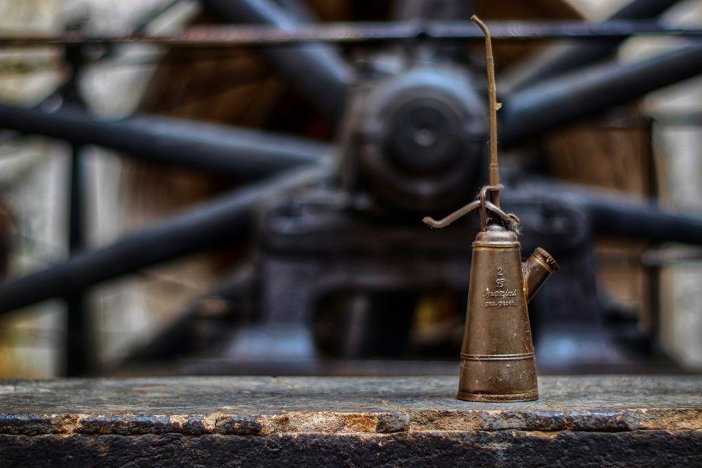 A classic metal oil can sits on a wall with a large wheel in the background.