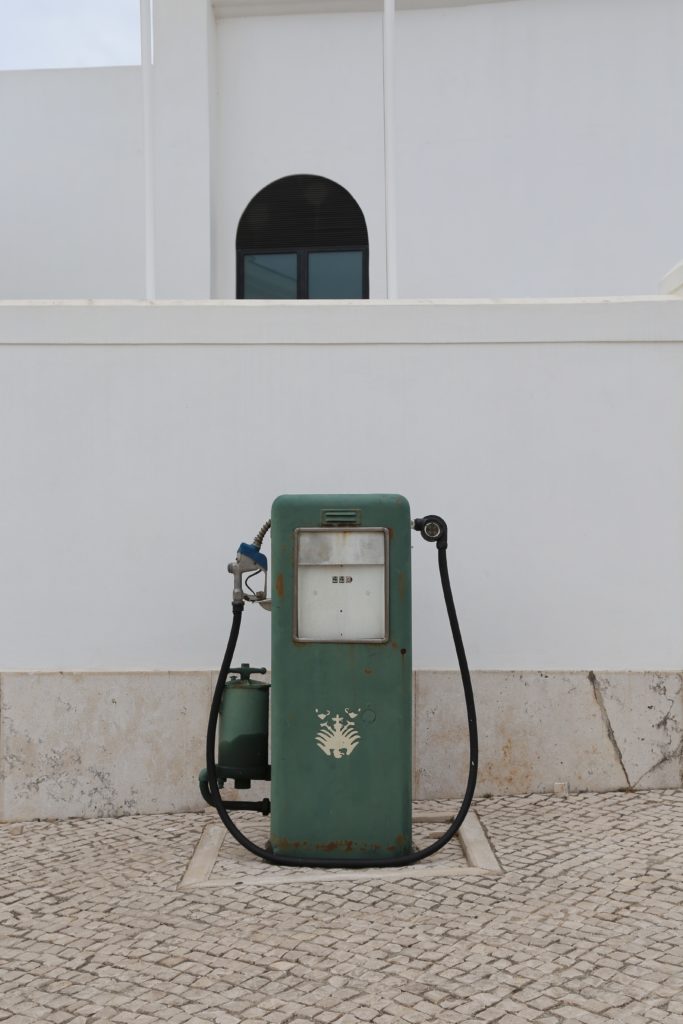 A green vintage fuel pump against a wall with a white building in the background.